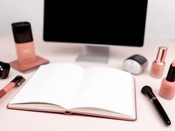 Offenes Notizbuch neben eleganten Beauty-Accessoires und einem Laptop auf einem hellen Tisch